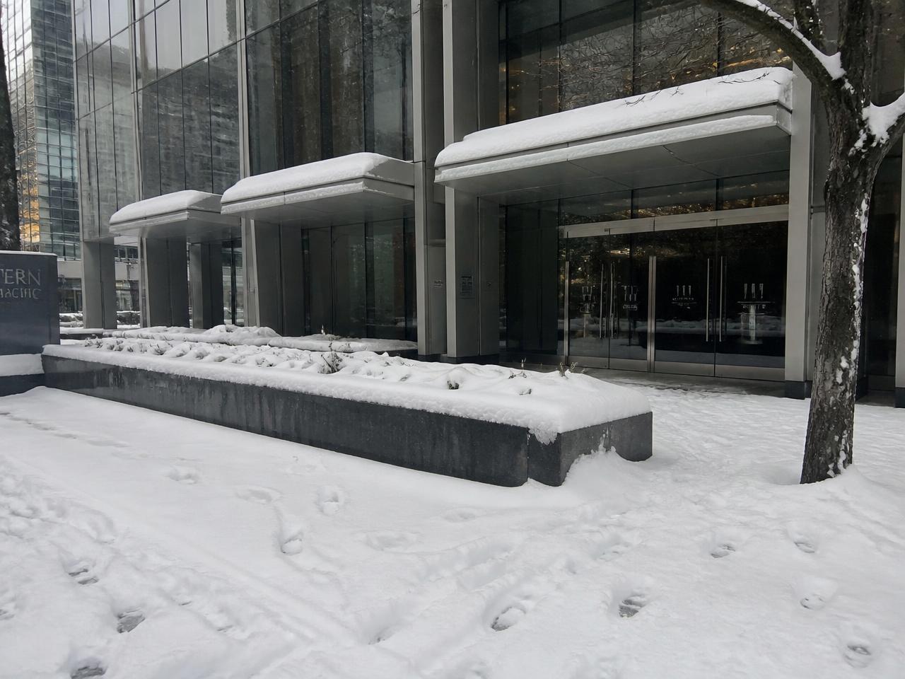 Snow accumulation across the entry, planters and public sidewalk of a downtown Vancouver commercial building before clearing